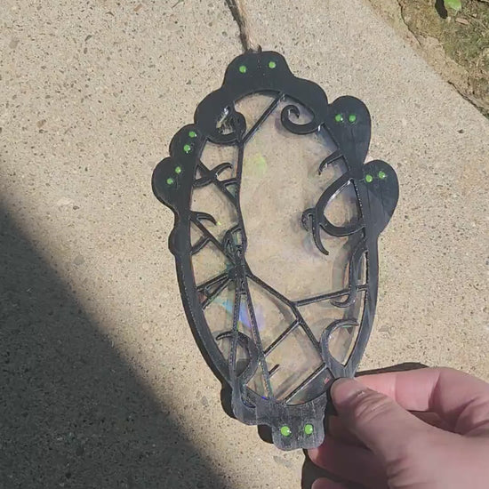 A black filament framed suncatcher is lifted to show rainbow effects from sunlight