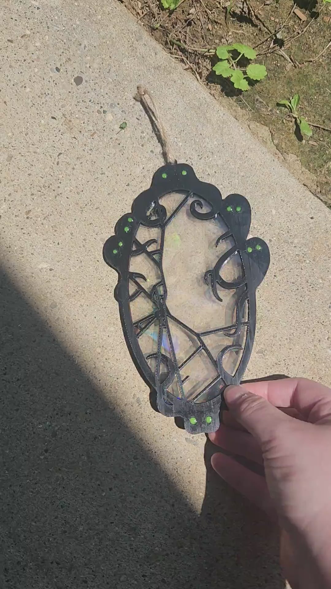 A black filament framed suncatcher is lifted to show rainbow effects from sunlight